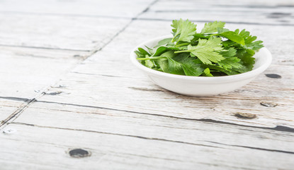 Fresh parsley leaves in white bowl over wooden background