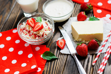 healthy breakfast of fruit and dairy products , cottage cheese with sour cream and milk, butter and roll , strawberries and syrup on a wooden background