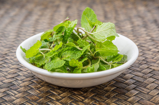 Fresh mint leaves in white bowl over wicker background
