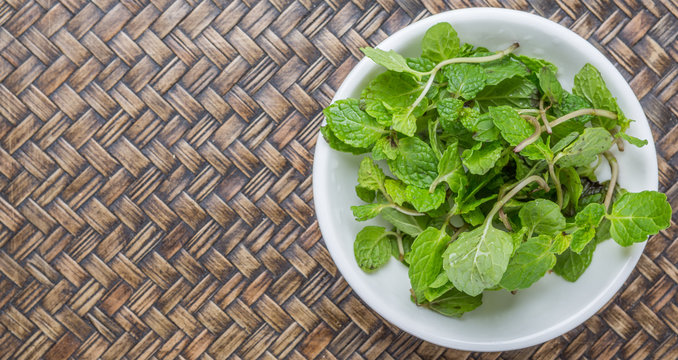Fresh mint leaves in white bowl over wicker background