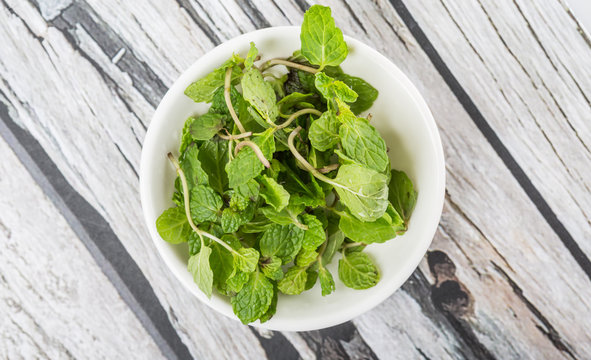 Fresh mint leaves in a white bowl over white background