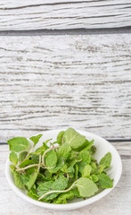 Fresh mint leaves in a white bowl over white background