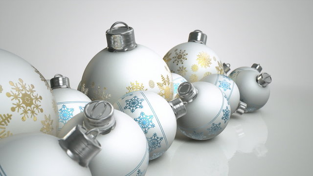 A macro pan of a collection of a mix of small and large matte white christmas baubles decorated with fine ornate snowflake patterns in gold and blue on an isolated white background