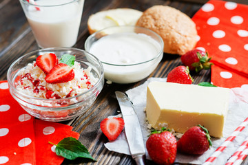 healthy breakfast of fruit and dairy products , cottage cheese with sour cream and milk, butter and roll , strawberries and syrup on a wooden background