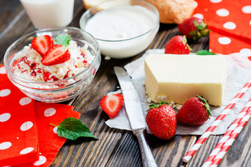 healthy breakfast of fruit and dairy products , cottage cheese with sour cream and milk, butter and roll , strawberries and syrup on a wooden background