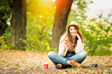 Beautiful young woman with smartphone in park in autumn