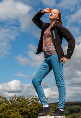14 year old girl standing on a rock posing with hand on hip against a summer sky