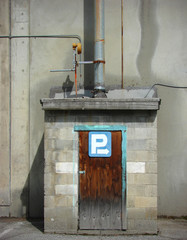 old cinder block industrial shed with pipes, wooden door and parking sign