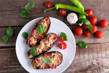 Dish of eggplant with cherry tomatoes and cheese in white plate on wooden table, top view