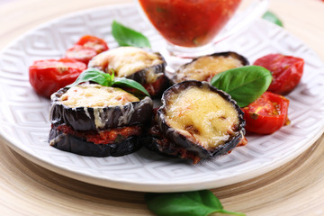 Dish of eggplant with cherry tomatoes and cheese in white plate on wooden table, closeup