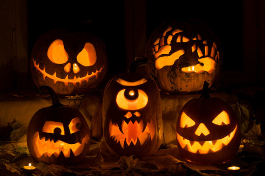Photo composition from five pumpkins on Halloween. Jack, terrible hands, embittered, a Cyclops and evil pumpkin against an old window, leaves and candles.