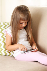 Beautiful little girl  with smart phone sitting on sofa, on home interior background