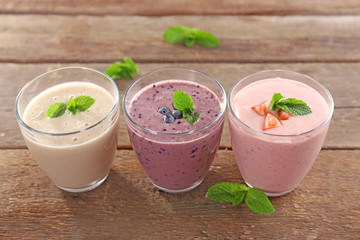 Tasty blueberry, strawberry and milk yogurts in a row on wooden background