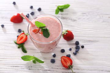 Fresh strawberry yogurt with berries around on light wooden background