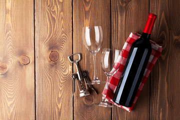 Red wine bottle, glasses and corkscrew on wooden table