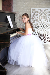 Attractive little princess girl in beautiful white dress plays piano