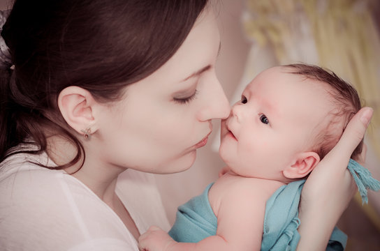 Mother kissing newborn baby on the background of crib