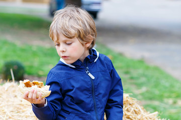 Adorable blond kid boy eating hot dog outdoors