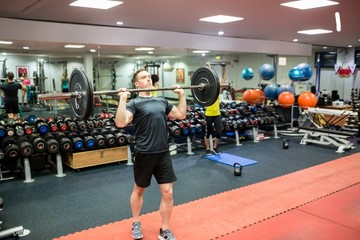 Fit man lifting heavy barbell in weights room