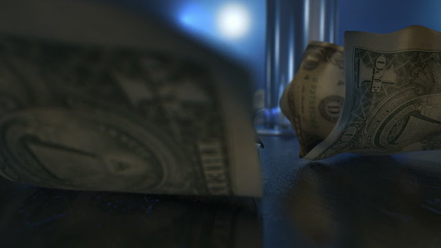An slow pan across an isolated stripper pole on a stage lit by spotlights surrounded by crumpled up one dollar bill tips on a blue strip club ambient background