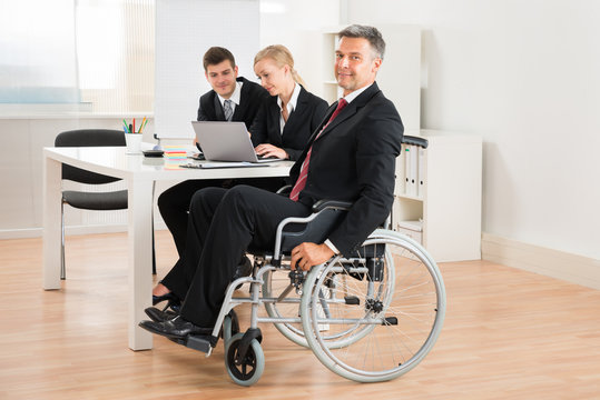 Businessman On Wheelchair With Colleagues In Office