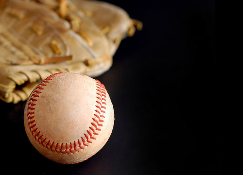 Old baseball glove and rough ball with side lighting on black