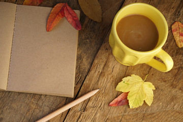 notebook and coffee on wooden table decorated with autumn leaves