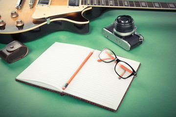Electric guitar with notepads, pencil, glasses and old camera on a green background. Filtered retro image