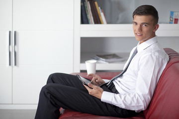 Happy young businessman with tablet at sofa in office sitting on
