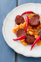 fried shrimps with sausages and red pepper on white plate on blue background