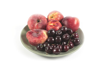 Ripe red peaches and cherry on a ceramic plate isolated on white