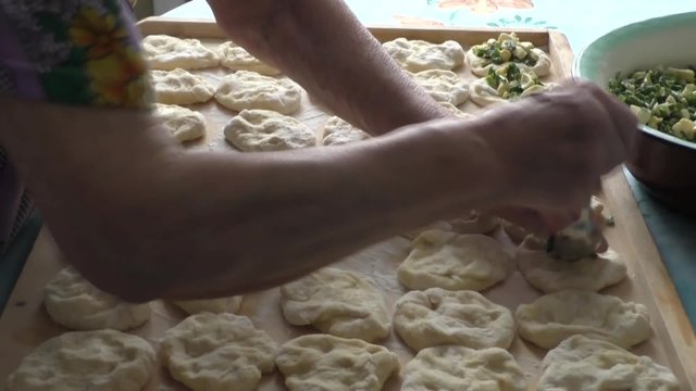 An elderly woman puts toppings on the dough