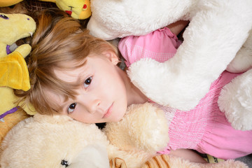 Little girl lies among stuffed toys