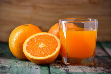 Orange juice glass and fresh oranges on wood