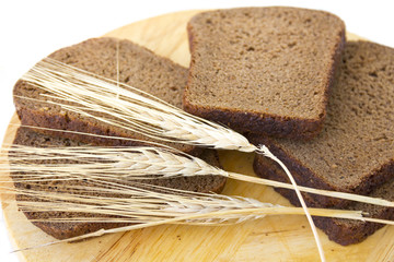 Slices of rye bread on a wooden board and ears of rye