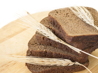Slices of rye bread on a wooden board and ears of rye
