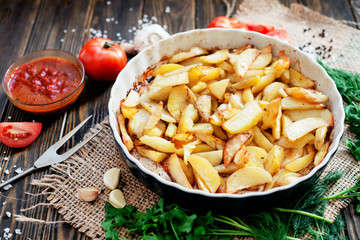 baked chicken legs in garlic marinade with baked potatoes , sauce , tomatoes , bread and herbs on wooden background