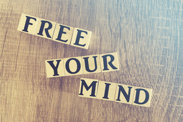 Free Your Mind message written with wooden blocks on a wooden table. Image cross processed for retro look