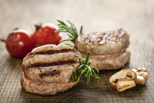 Gegrillte Schweinemedaillons an Gem&uuml;se auf rustikalem Holzbrett