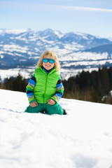 Fototapeta na wymiar Happy little boy in sunglasses in winter mountains on a sunny day