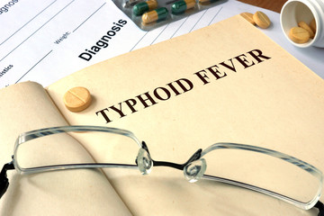 Word  Typhoid Fever on a paper and pills on the wooden table.