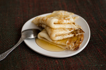 Three pancakes with honey on a white plateau with a spoon. Pancakes with honey on a white plateau