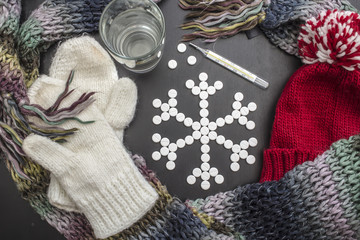 concept snowflakes made from medicinal tablets, lie close colorful winter clothes, a glass of water and a thermometer.