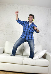 20s or 30s man jumped on couch listening to music on mobile phone with headphones playing air guitar