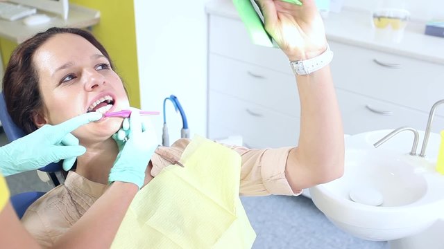 Female dentist showing to her sitting and looking at a mirror female patient how to use dental interproximal brush correctly / camera moving left / close-up