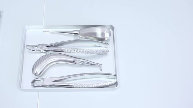 Steel dental instruments in a silver trays over white countertop / camera moving left