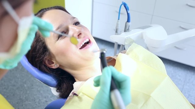 Female dentist wearing medical mask and gloves starting polishing female patient's teeth / camera moving right / close-up