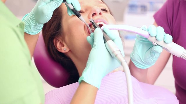 Female dentist and her assistent starting to work on teeth of woman sitting in a dental chair / camera moving left