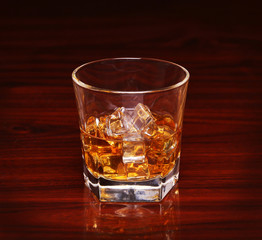 Glass of alcohol scotch whiskey with ice cube on wooden table an