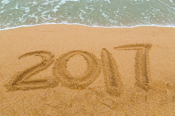 2017 inscription written on sandy beach with wave approaching